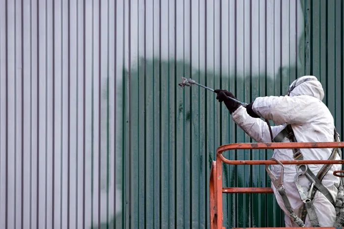 A painter spraying coating onto corrugated metal sheeting from a lift